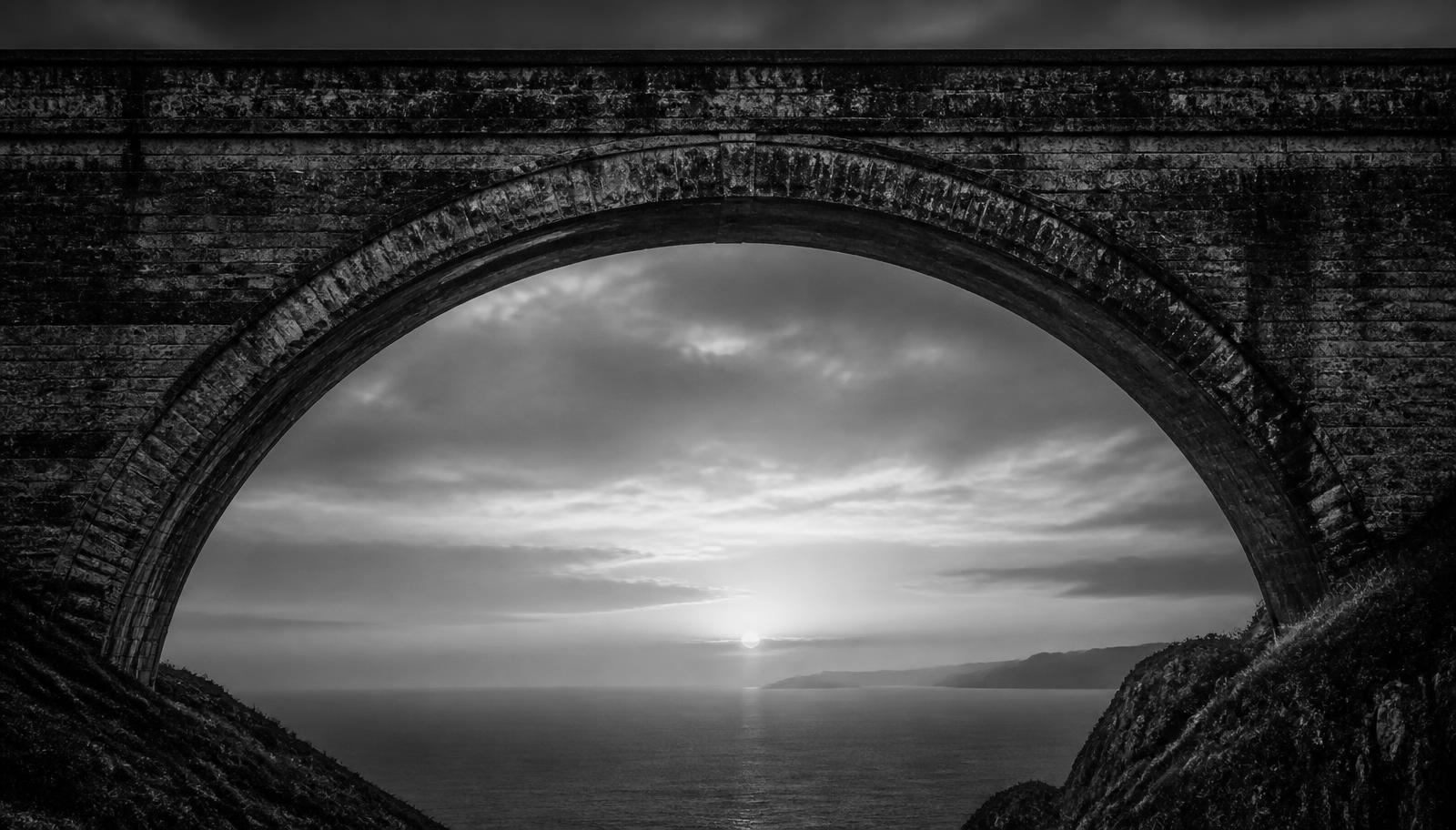 A weathered stone bridge arch spanning a misty Atlantic horizon at first light